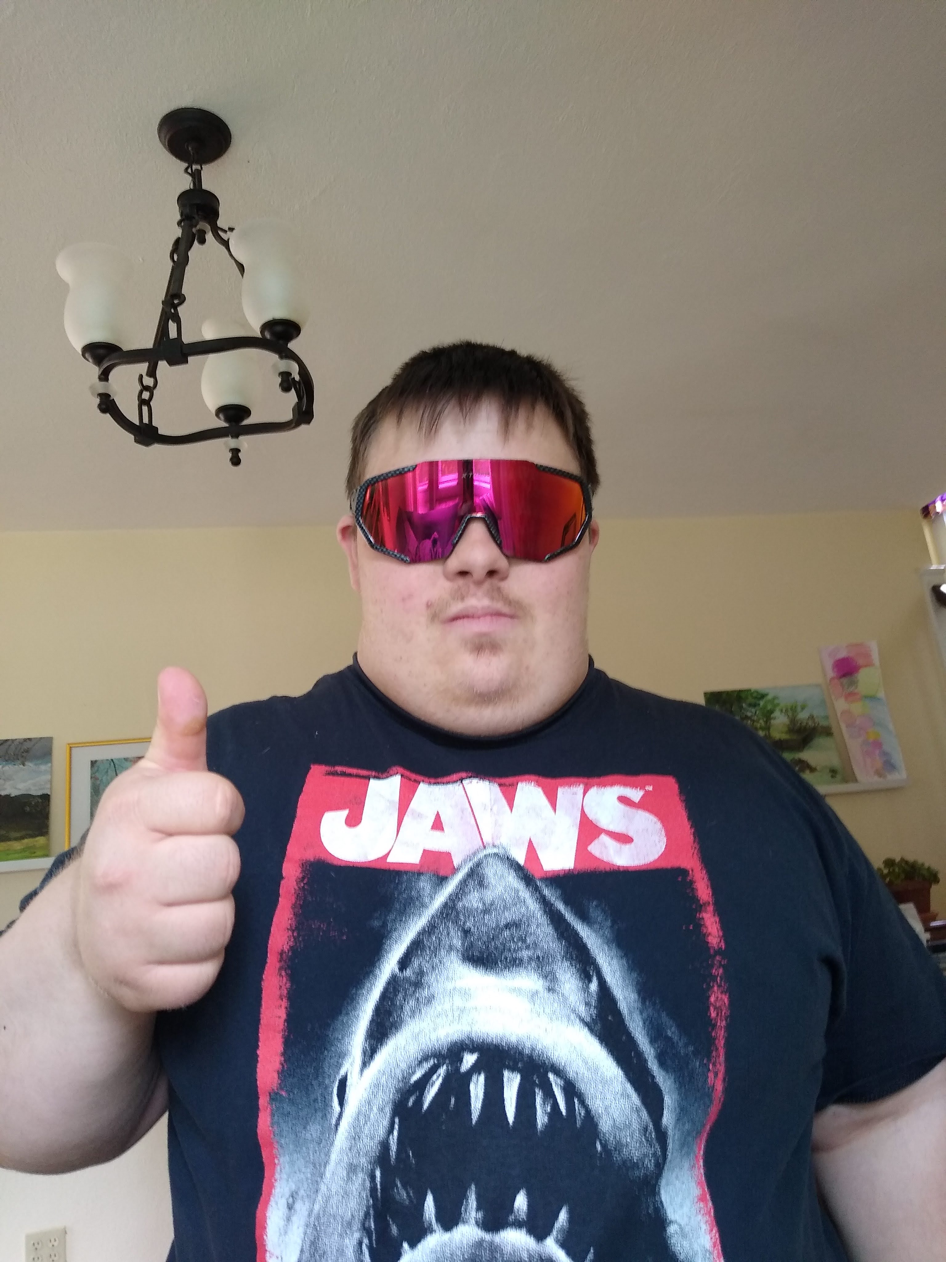 Eliot in a Jaws t-shirt and pink wraparound sunglasses, giving a thumbs up
